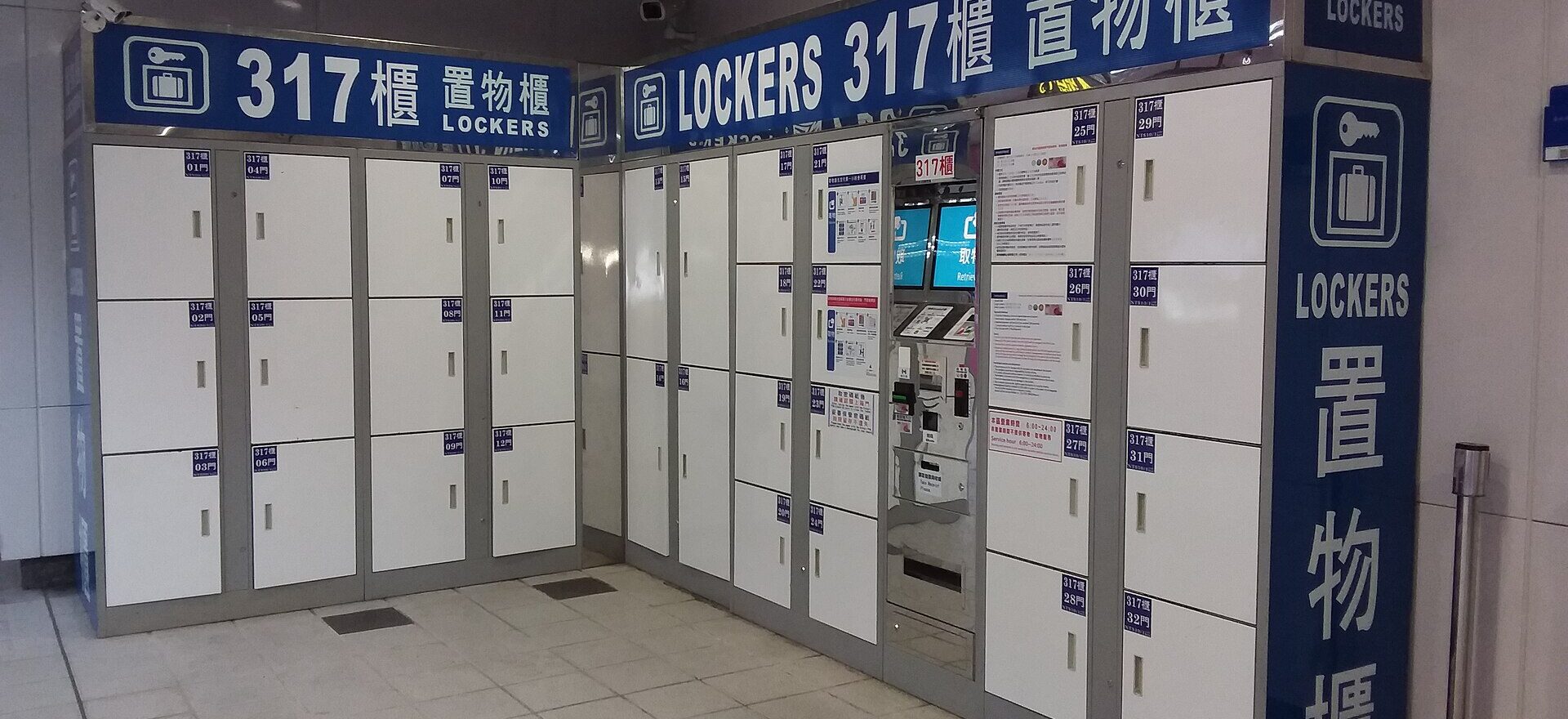White luggage lockers with blue bilingual signs and a payment terminal at Taipei 101/World Trade Center MRT station.