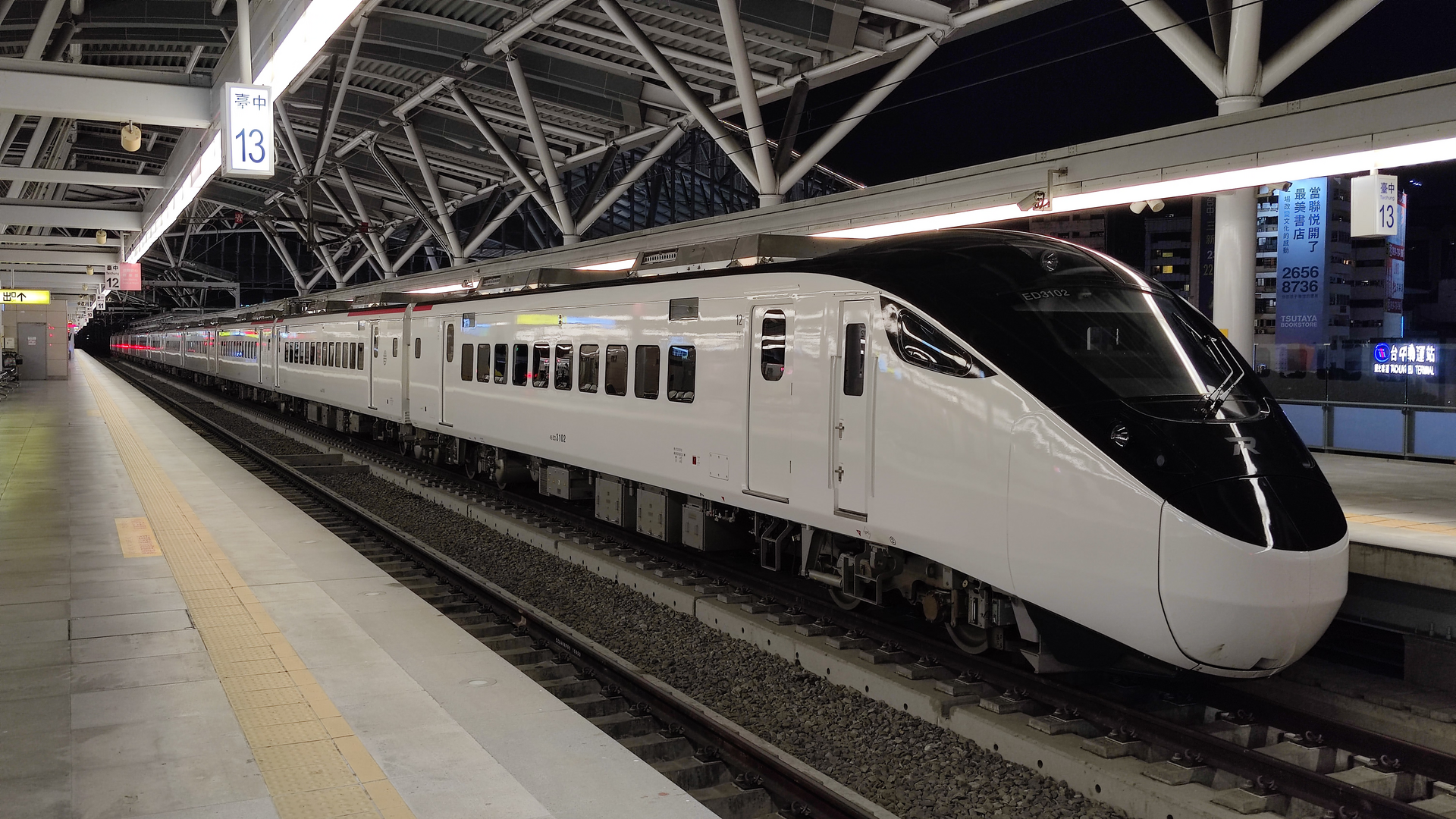 A white Taiwan Railways EMU3000 express train stands beneath the steel platform roof at Taichung station at night.
