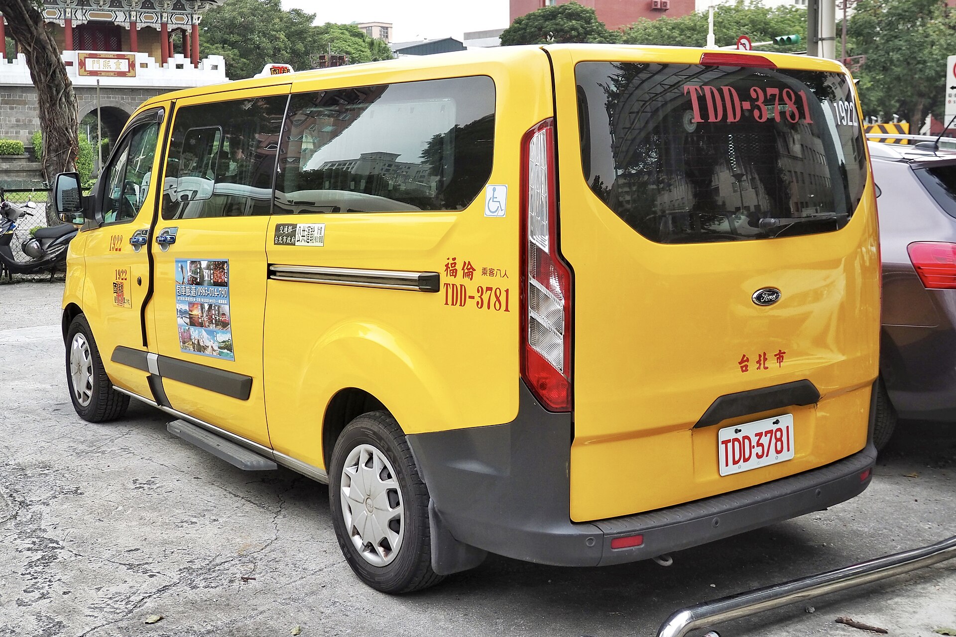 Yellow Ford taxi van in Taipei with a wheelchair symbol beside its sliding door and a rear window fleet number.