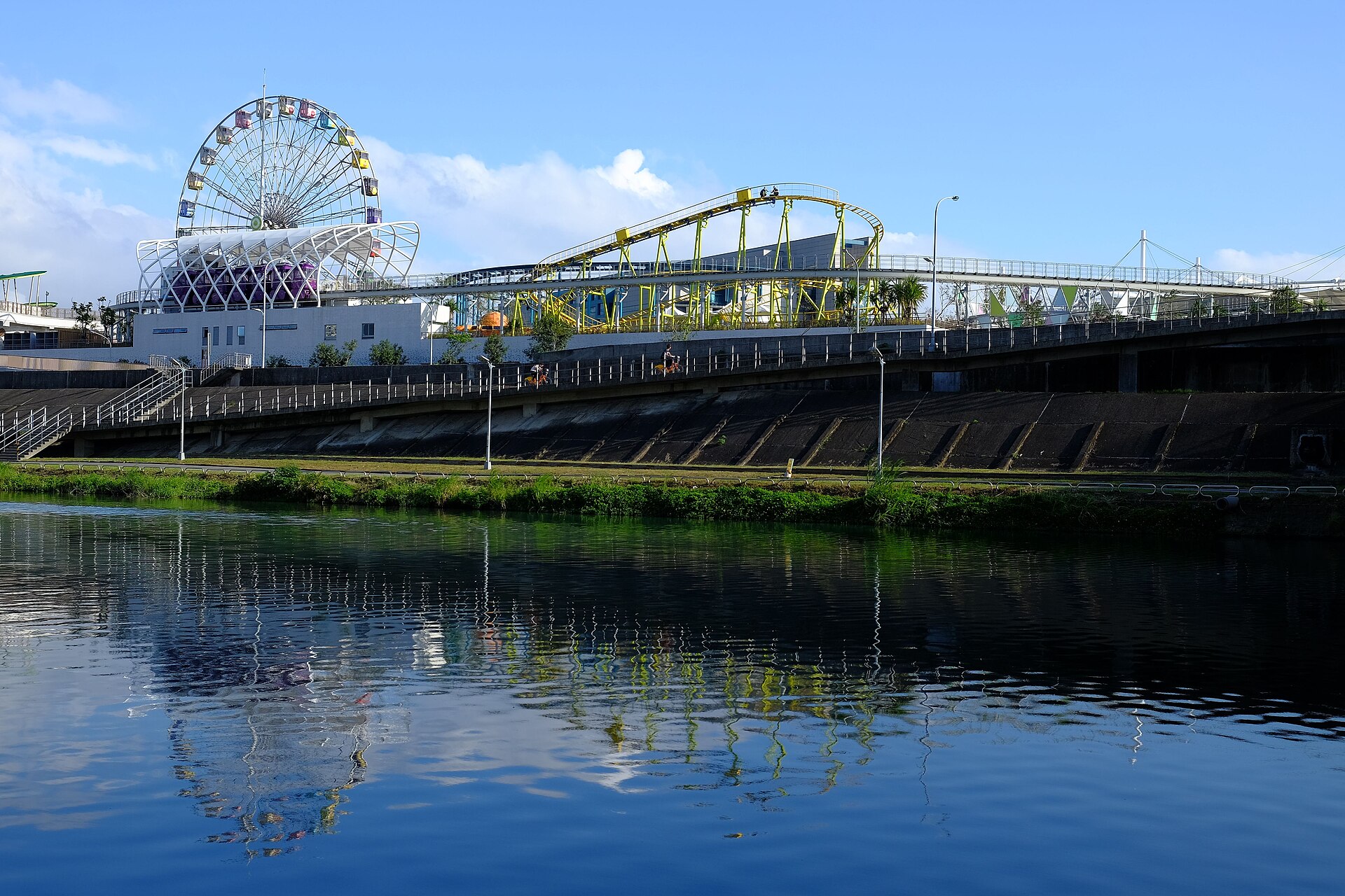 Yellow roller coaster track curves beside the Ferris wheel at Taipei Children's Amusement Park, with reflections in the river.